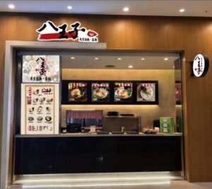 八王子東京拉麵店面以木質基調搭配紅黑配色招牌，東京拉麵、丼飯字樣相當搶眼。(圖／食現餐飲集團)